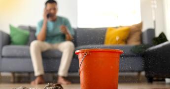 wiadro, do którego kapie woda. W tle mężczyzna dzwoniący przez telefon.