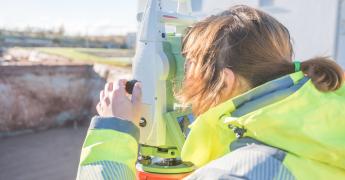 Kobieta w żółtej kurtce. Spogląda przez tachimetr.