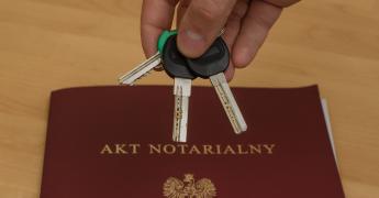 Klucze w dłoni na tle aktu notarialnego.