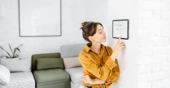 Kobieta trzymająca palec na panelu sterującym na ścianie. W tle kanapa.