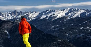 Sylwetka odwróconej osoby, która zjeżdża na snowboardzie. W tle góry.